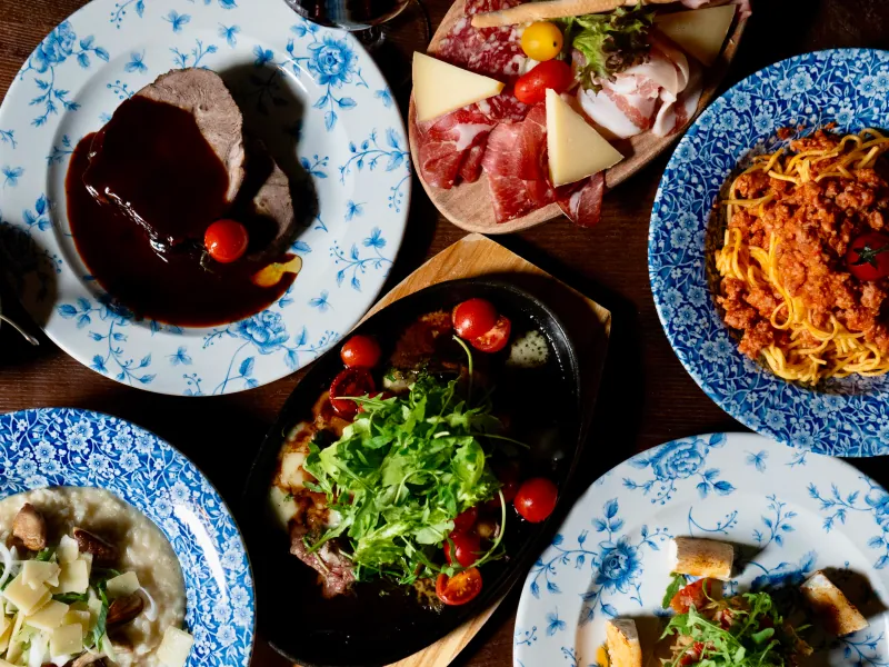Gedeckter Tisch von oben: Pasta, Tatar, Antipasti und Risotto auf blau gemusterten Tellern.