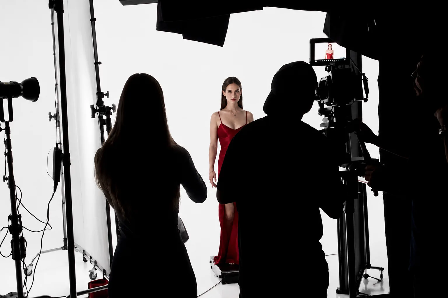 Fotoshooting im Studio: Model im roten Kleid vor weisser Hohlkehle, Crew im Gegenlicht als Silhouette.